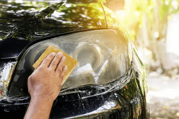 A person cleaning the car headlights with a sponge