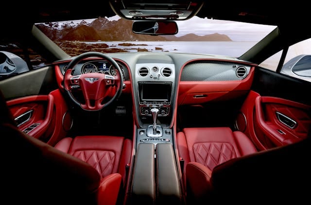 Luxurious red and black leather interior of a Bentley car with a scenic ocean and mountain view visible through the windshield.